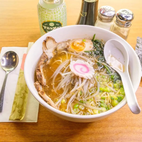 A bowl of ramen with pork, egg, bean sprouts, scallions, and a fish cake, next to a melon soda.