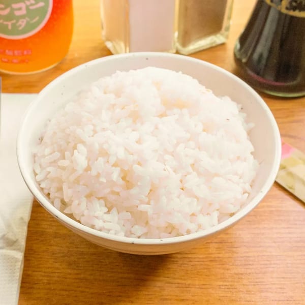 A white bowl filled with fluffy white rice sits on a wooden table.