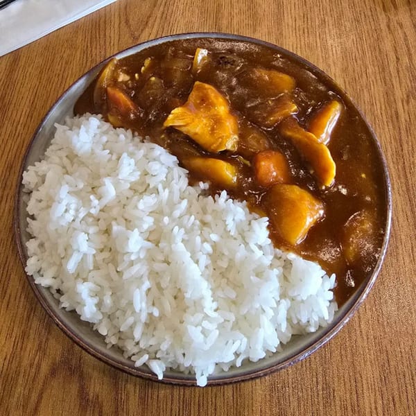 A plate of Menkoi's Japanese curry with white rice and chunks of chicken and vegetables.