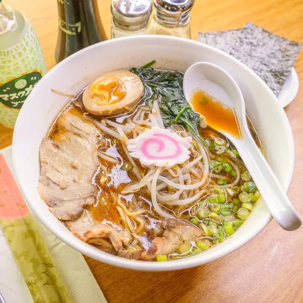 A bowl of ramen with pork, egg, narutomaki, bean sprouts, spinach, and green onions.