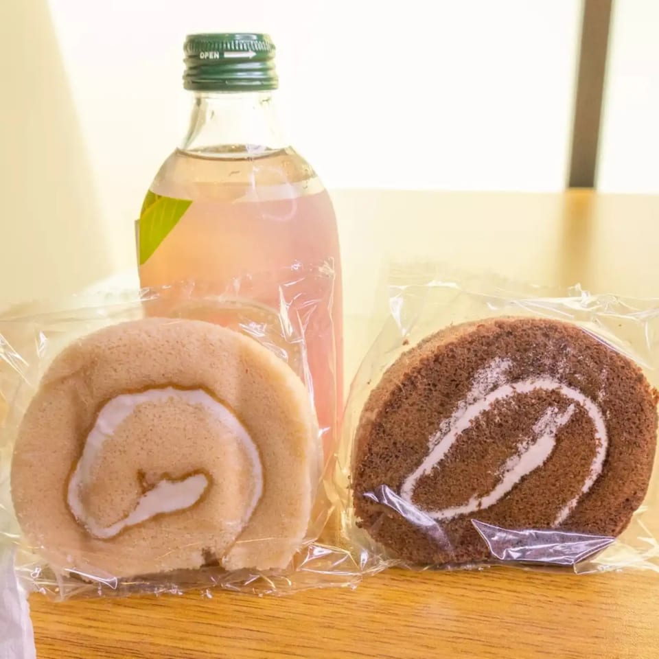 Two individually wrapped swiss rolls, one vanilla and one chocolate, with a pink drink bottle.