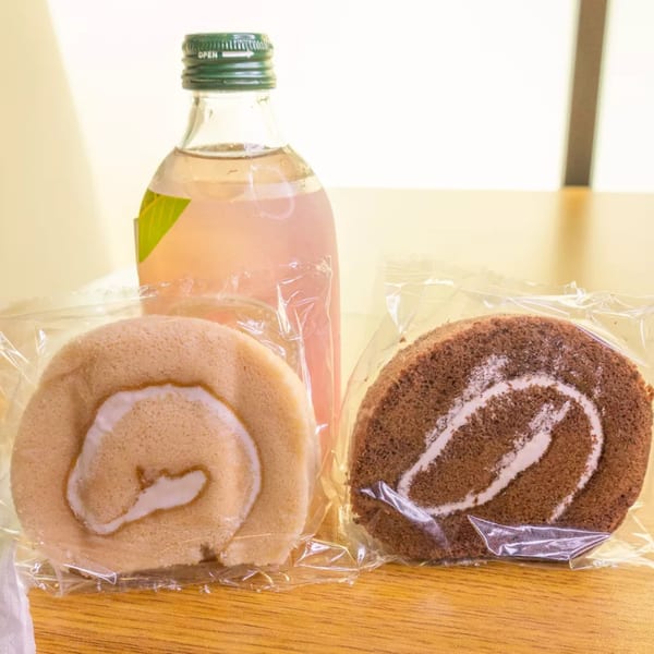 Two wrapped swiss rolls, one vanilla and one chocolate, with a bottle of pink soda.