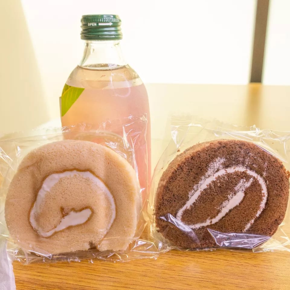 Two wrapped swiss rolls, one vanilla and one chocolate, with a bottle of pink soda.