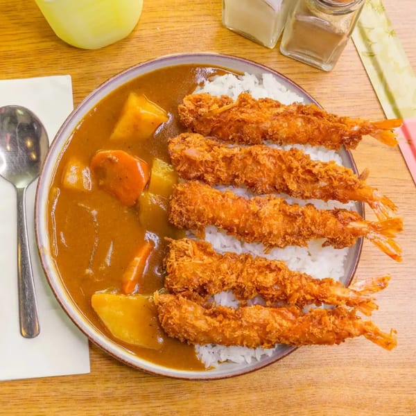 A bowl of Japanese curry with rice and five crispy fried shrimp on a wooden table.