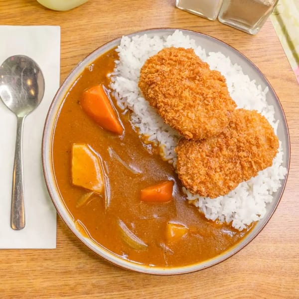 Top-down view of a plate of Japanese curry with rice and two crispy fried cutlets.